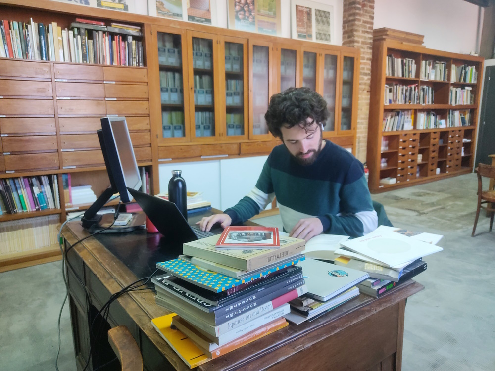 L’estudiant de màster treballant en un escriptori ple de llibres i un ordinador.