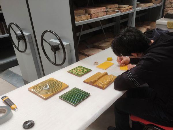 Taula amb peces de revestiment i home d'esquenes omplint fitxes d'inventari