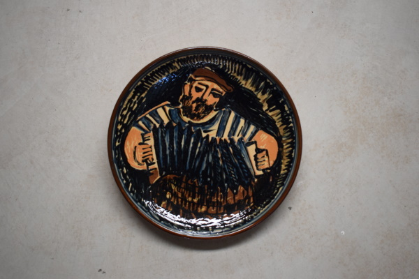 Plata de l’acordionista. Terra vermella, engalbes i vernís. Motlle. Decoració a pinzell. Josep Vilà Clara, 1973. Ø 35 cm. Col·lecció particular.