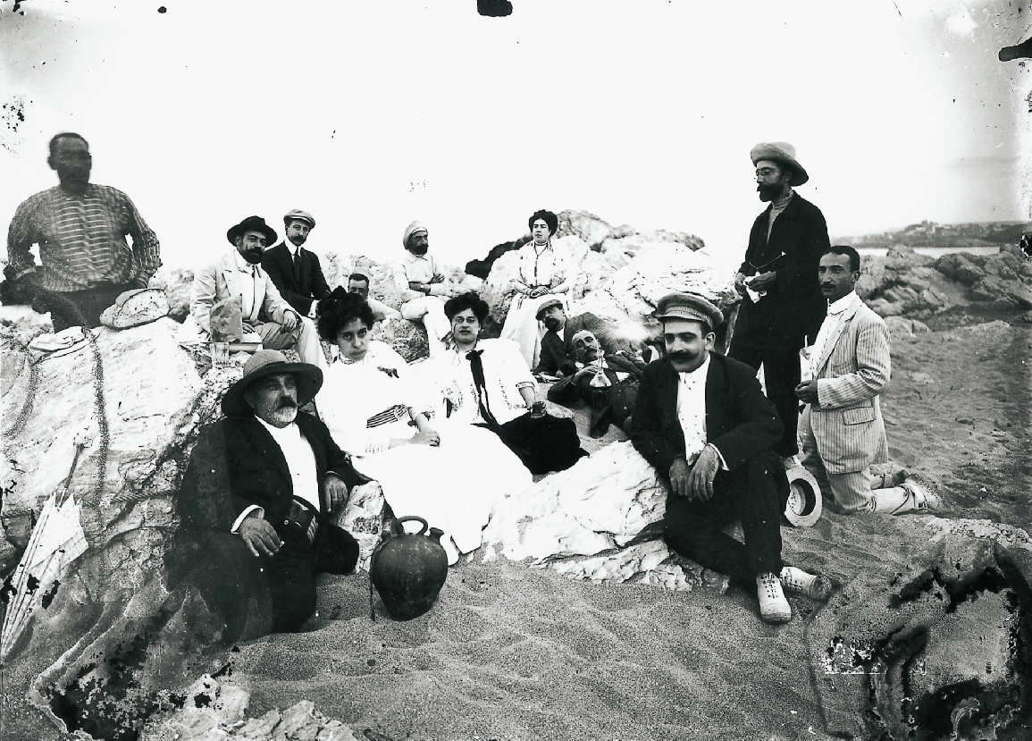 Grup de visitants de les ruïnes d'Empúries dinant a la platja (l'Escala, 1910). Autor: Josep Esquirol Pérez. Fons Esquirol MASLE - Arxiu Municipal de l'Escala