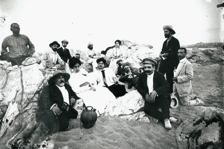 Grup de visitants de les ruïnes d'Empúries dinant a la platja (l'Escala, 1910). Autor: Josep Esquirol Pérez. Fons Esquirol MASLE - Arxiu Municipal de l'Escala